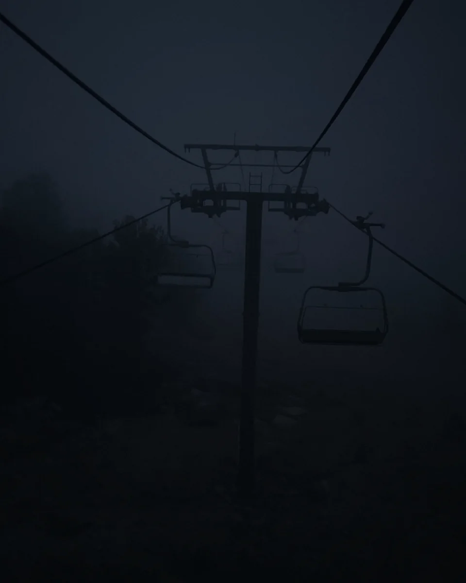 Empty chairlift seats disappearing into fog at dusk