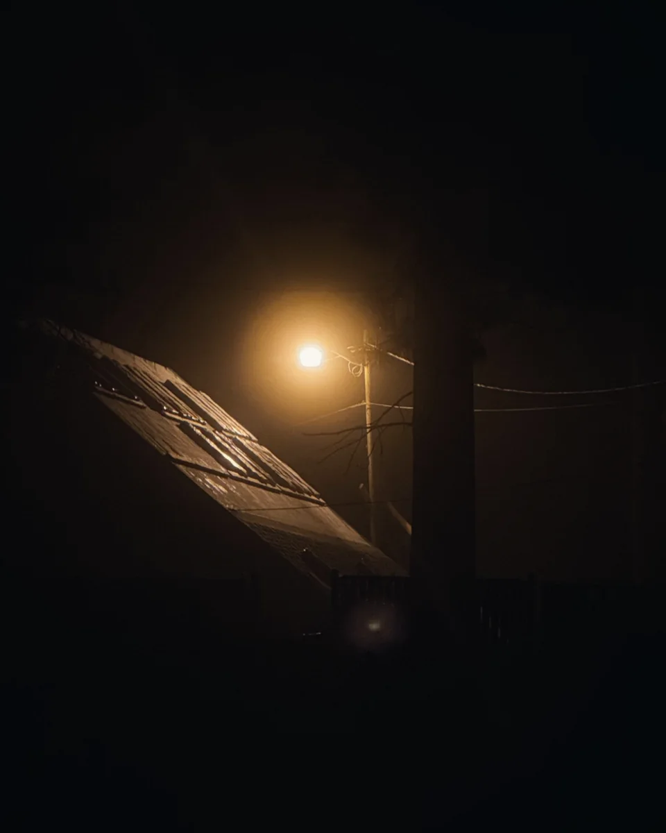 A streetlamp glowing through fog above a dark roofline