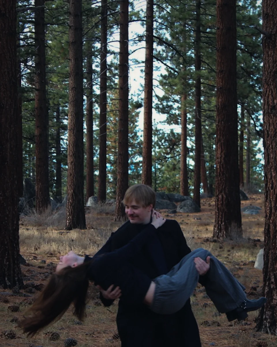 A man carrying a woman through a pine forest