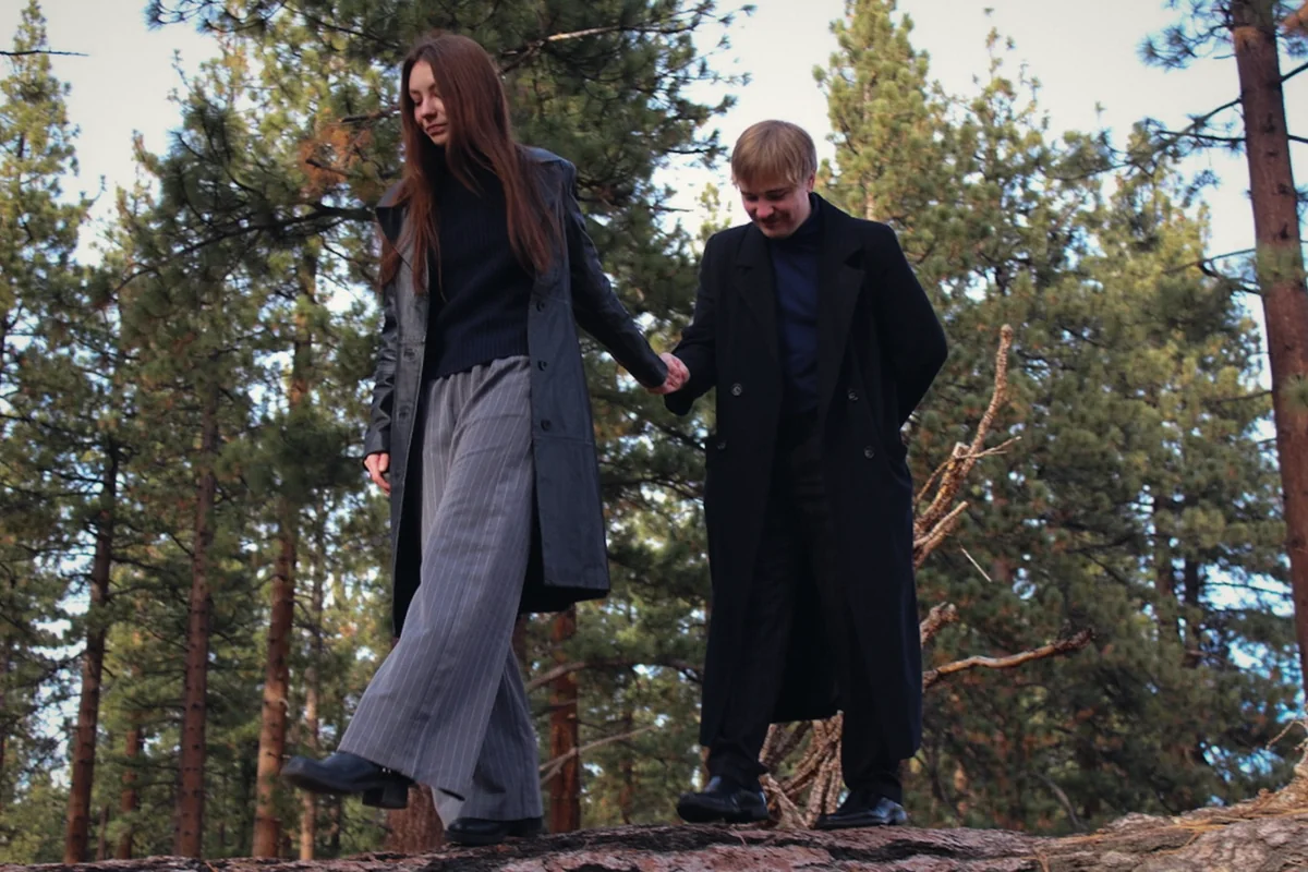 A couple in long coats walking hand in hand on a rock ledge