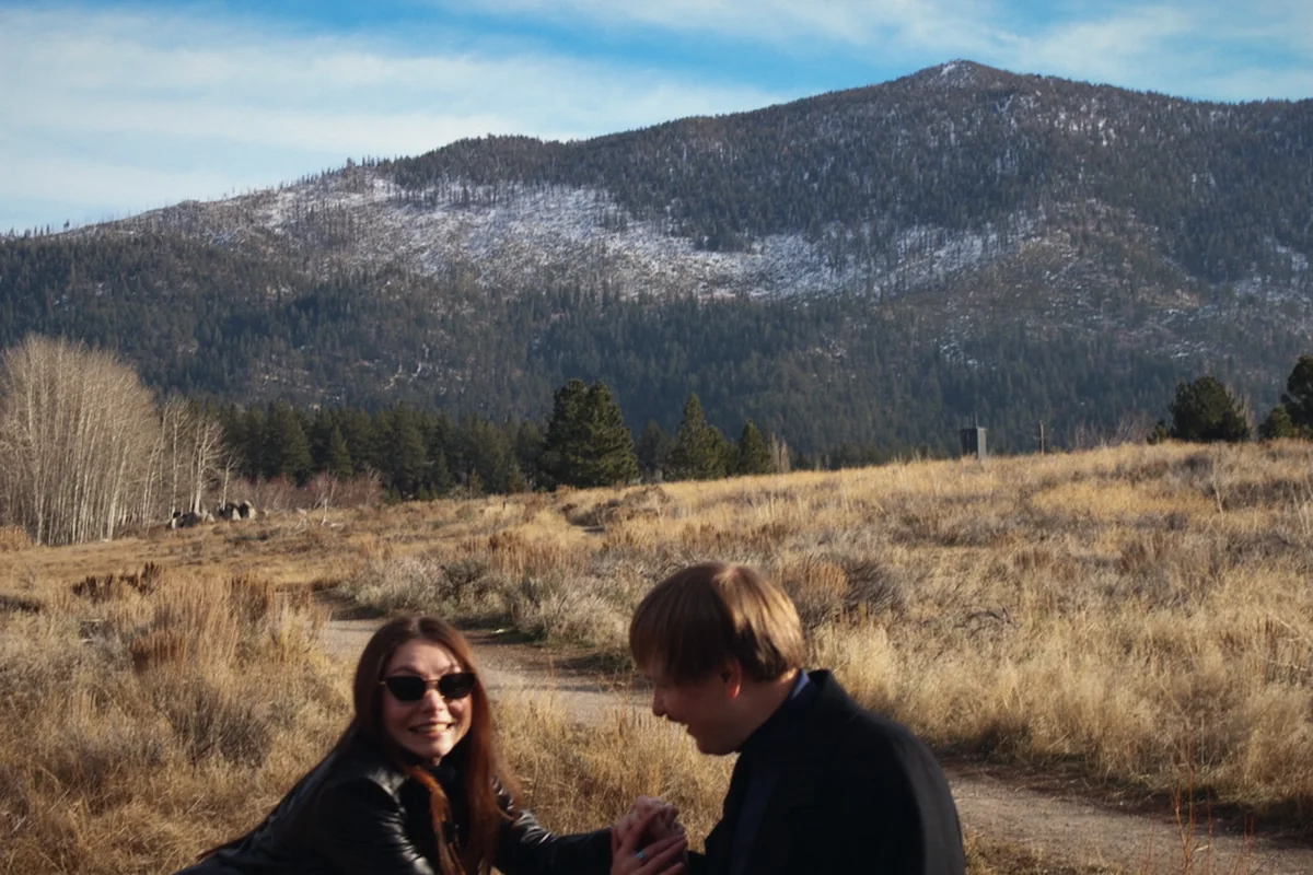 A couple laughing in a dry meadow below a mountain