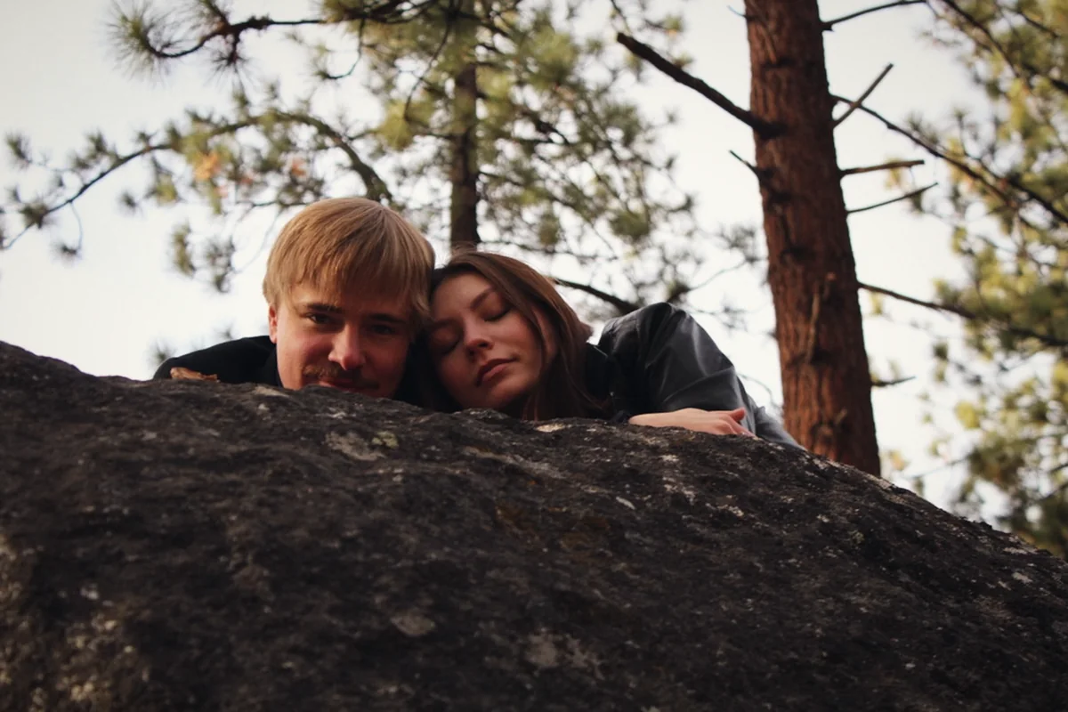 A couple resting their heads on a granite boulder
