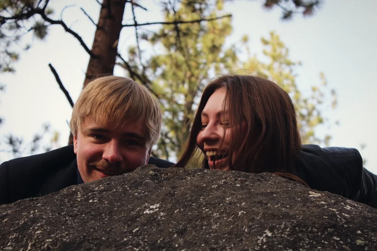 A couple laughing behind a granite boulder