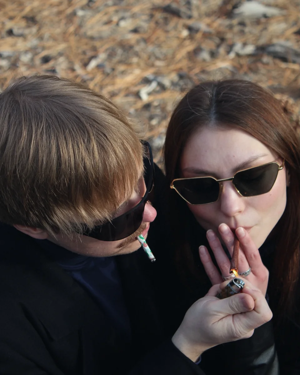 A couple in sunglasses sharing a lighter, close-up